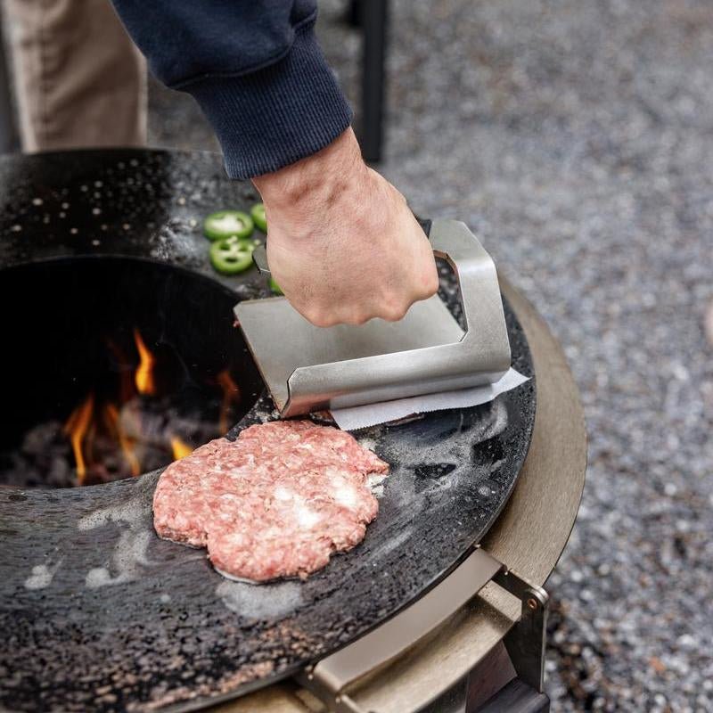 This is an image of someone pressing a smash burger with a Breeo Griddle Press