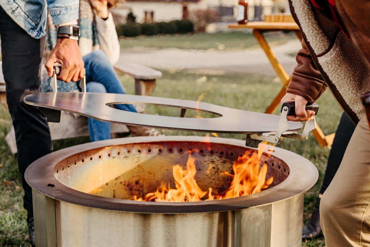 This is an image of two people removing the Breeo Searplate Griddle from the X30 firepit