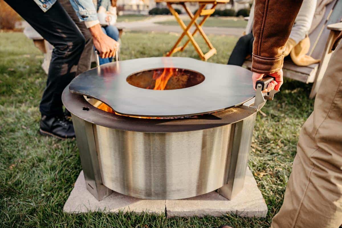 This is an image of two people removing the Breeo Searplate Griddle from the X3 firepit