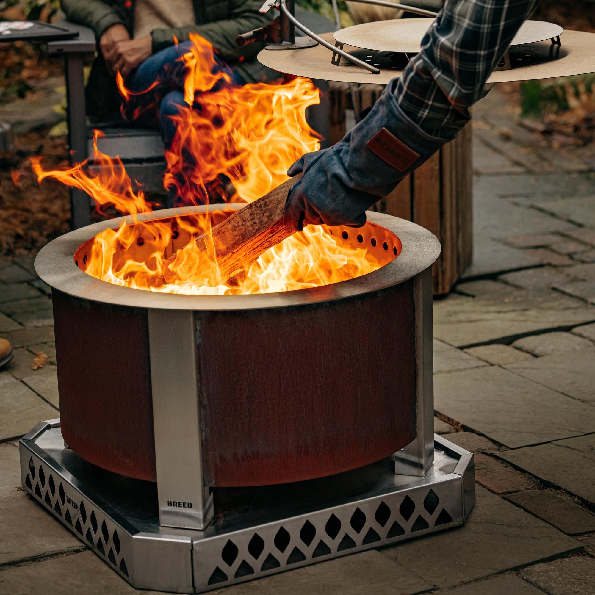 An image of a log being tossed in the fire with a Breeo X Series 24 firepit and Base.