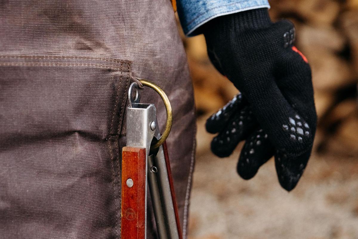 An image of tongs hanging from the D-ring on the waxed canvas apron