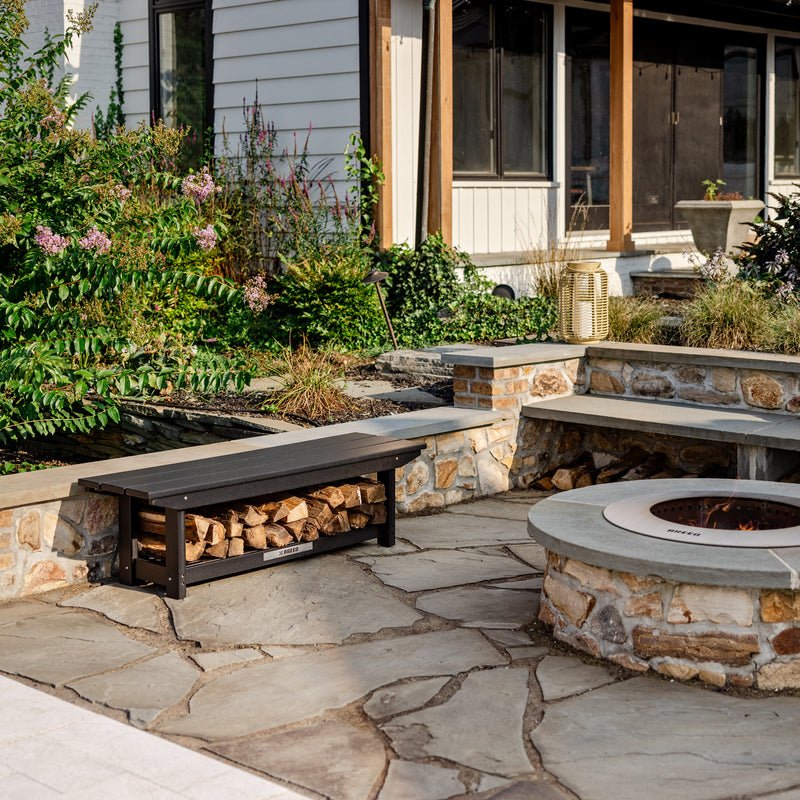 An X Series bench with firewood stacked underneath next to a Zentro firepit