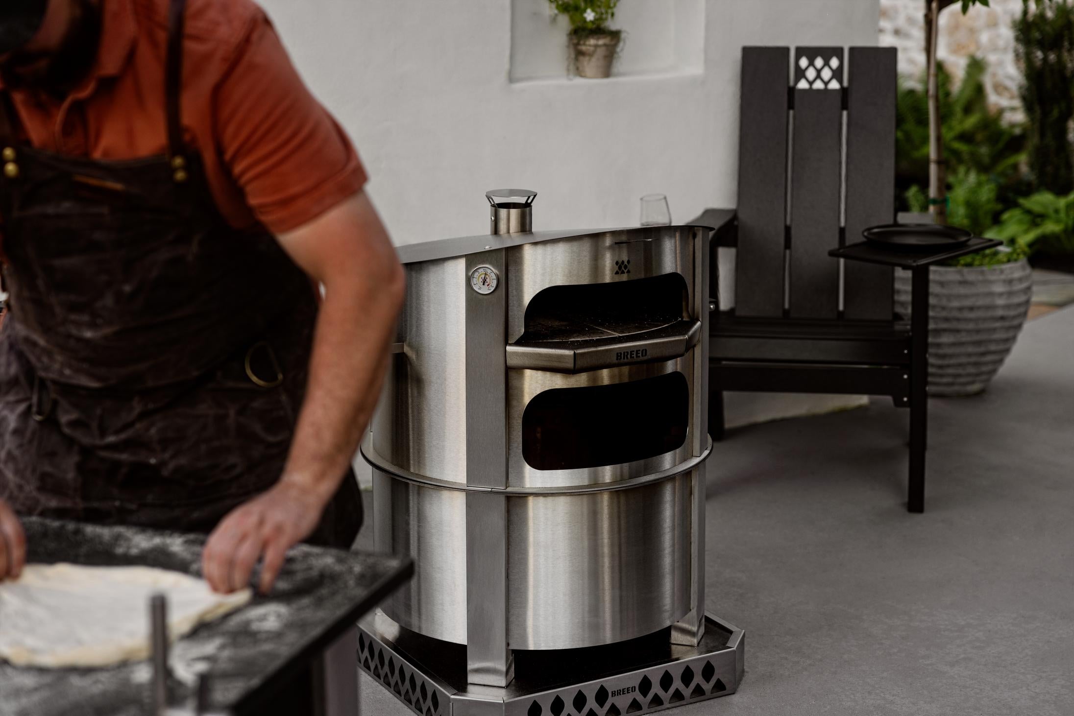 This is an image of a man rolling out dough in front of the Breeo Pizza Oven