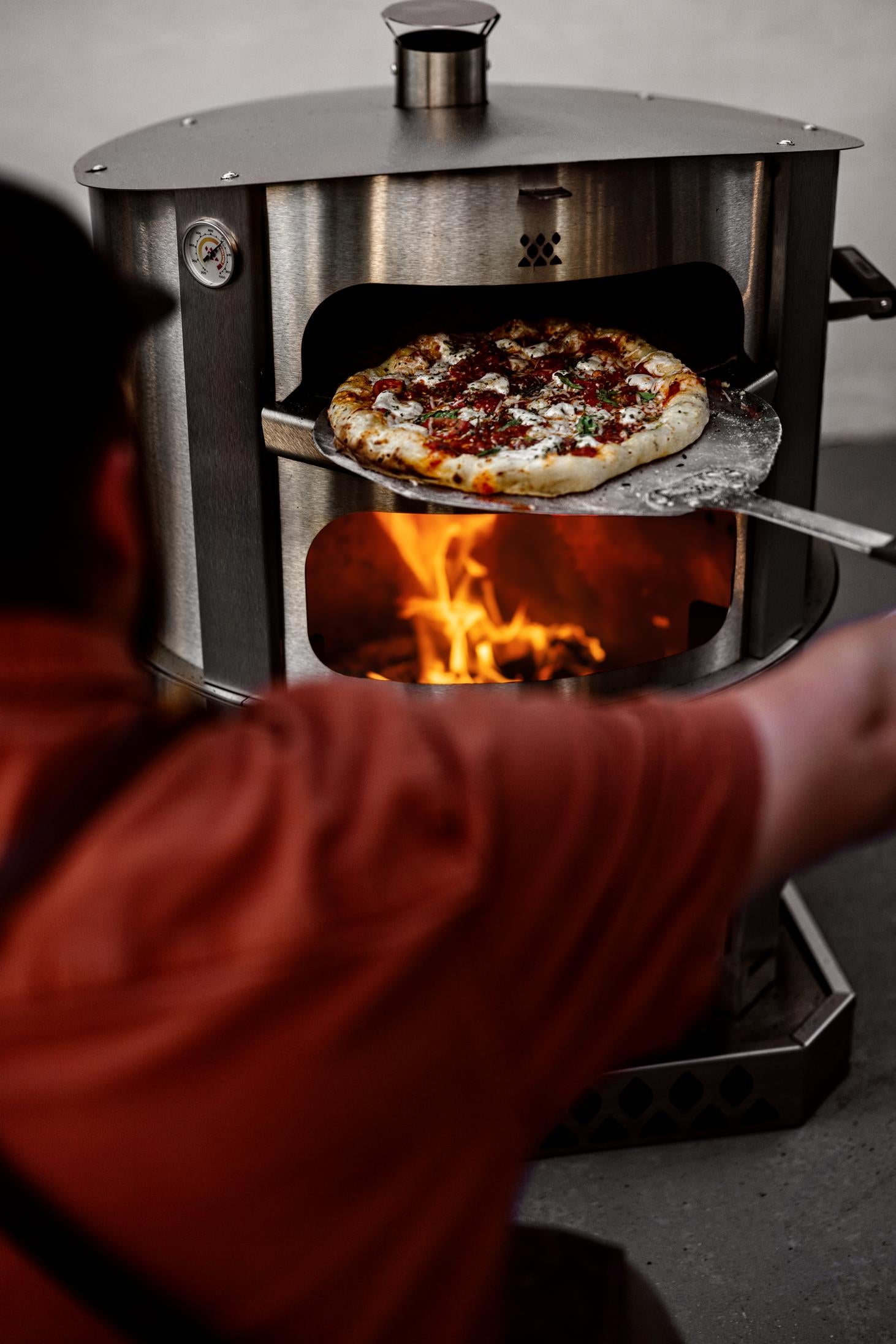 This is an image of a man removing a pizza from the Breeo Pizza Oven using a Pizza Peel