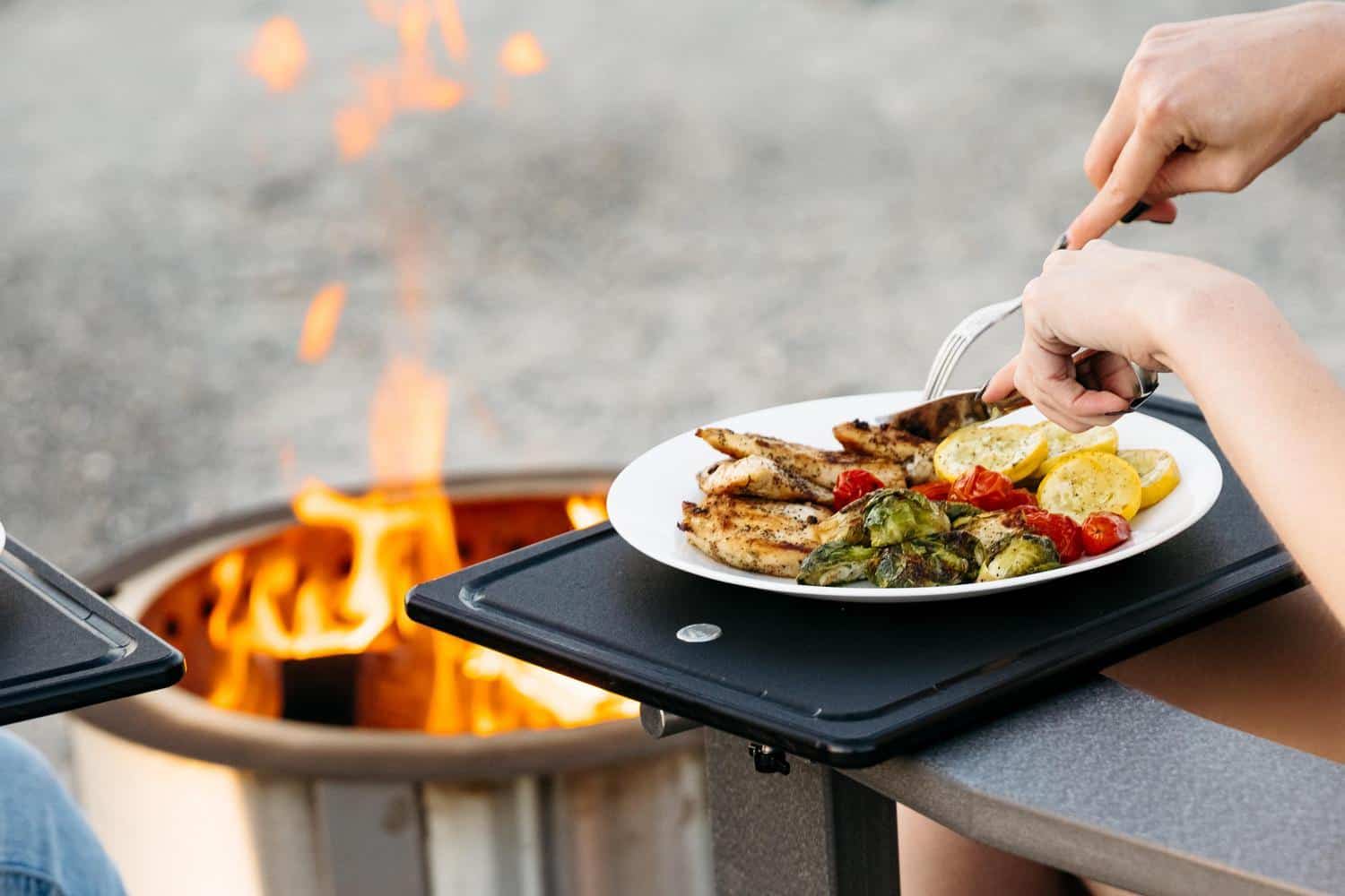 This is an image of someone eating grilled chicken on a Breeo Outrig Tray