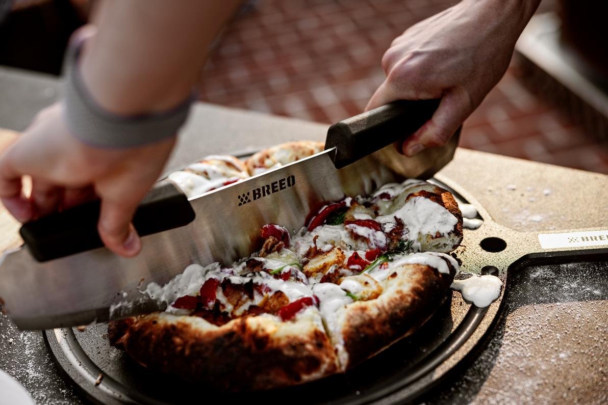 This is an image of the Breeo Pizza Rocker used to slice a pizza on the Serving Board