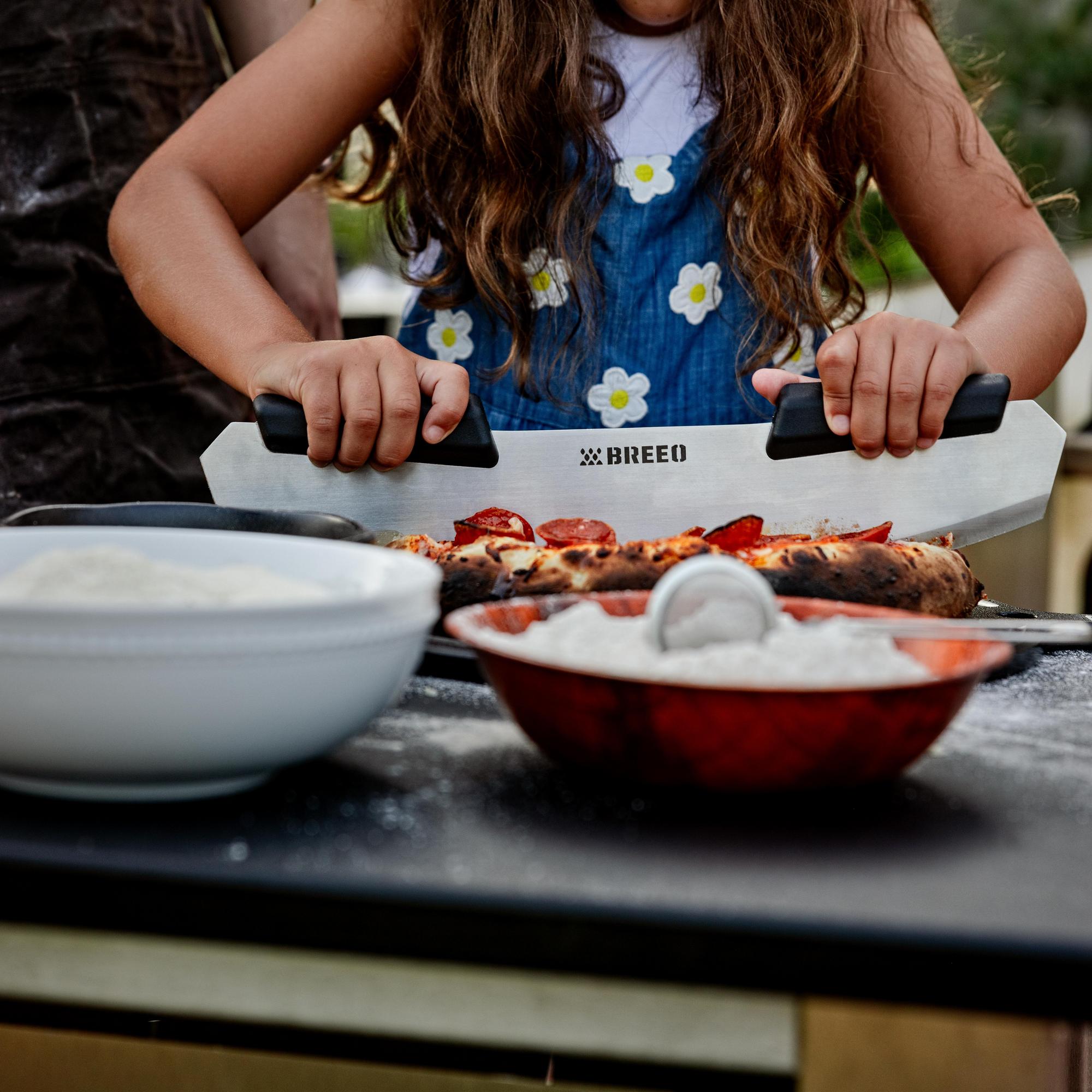 This is an image of a girl using the Breeo Pizza Rocker to slice Pizza