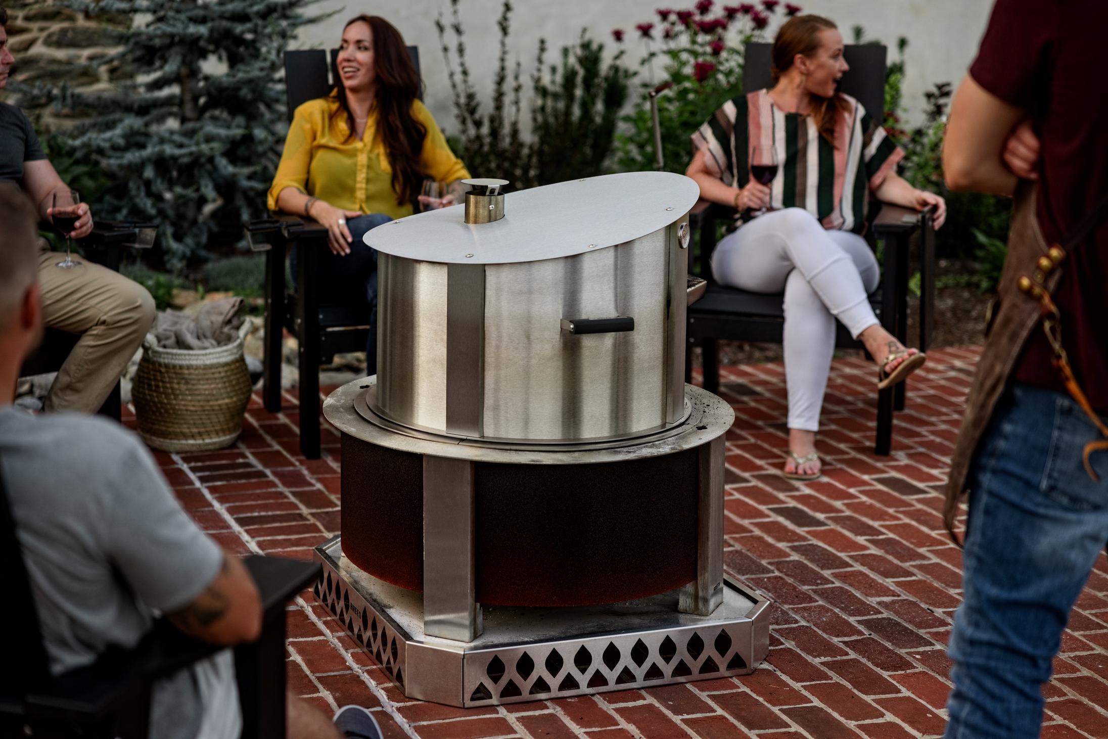 This is an image of a group of people sitting around a fire with a Breeo Pizza Oven