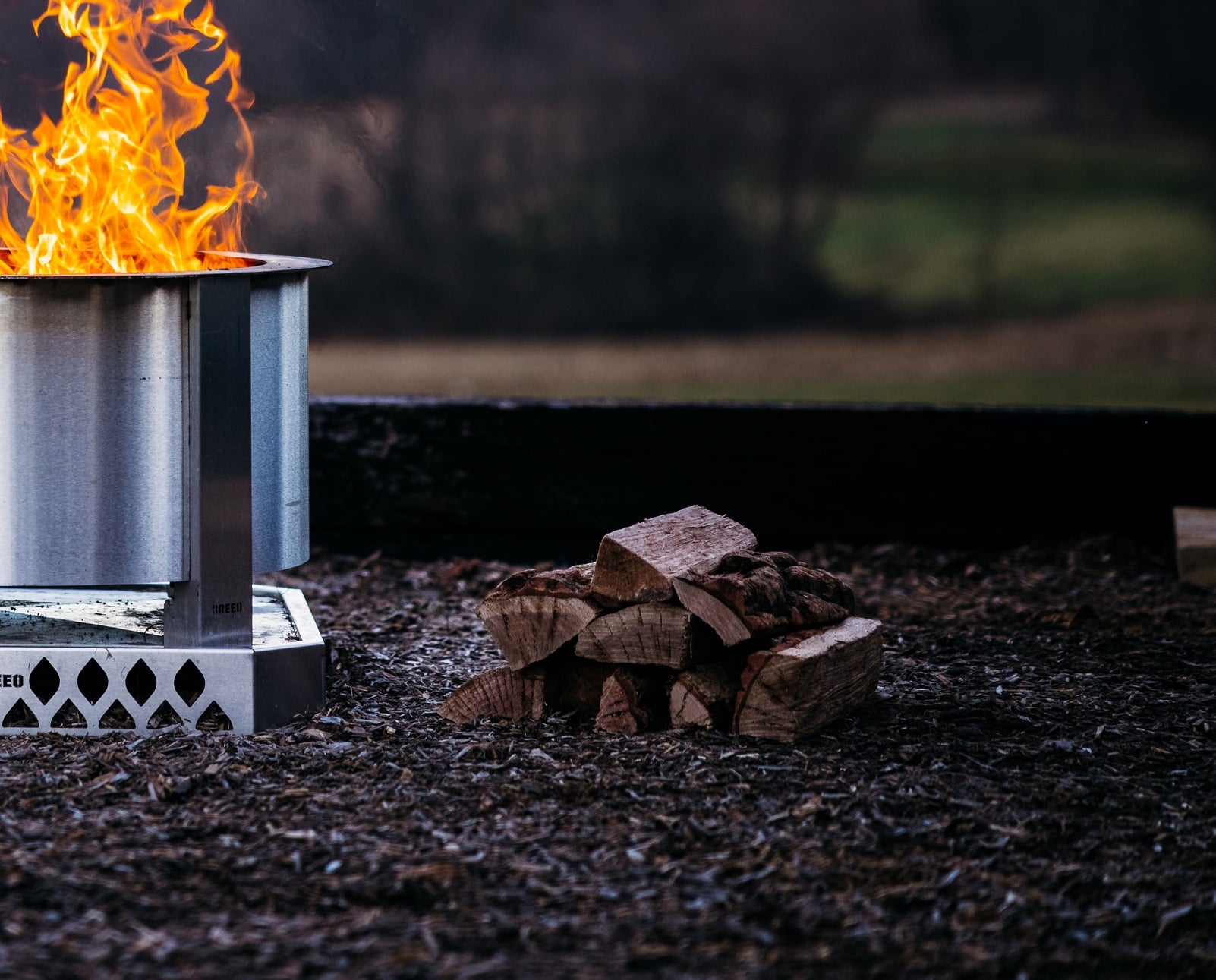 A pile of oak firewood next to a Breeo Firepit