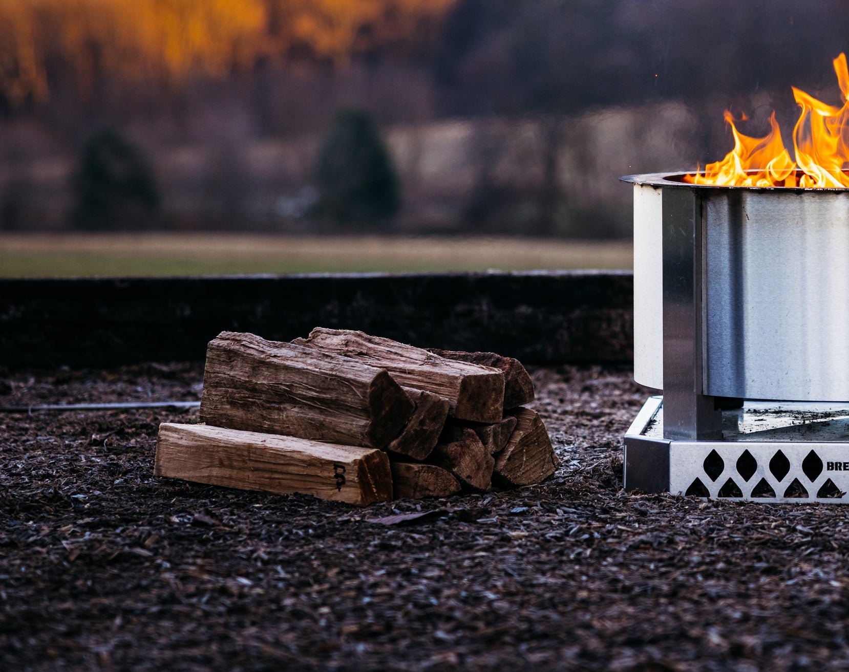 A pile of oak firewood next to a Breeo firepit
