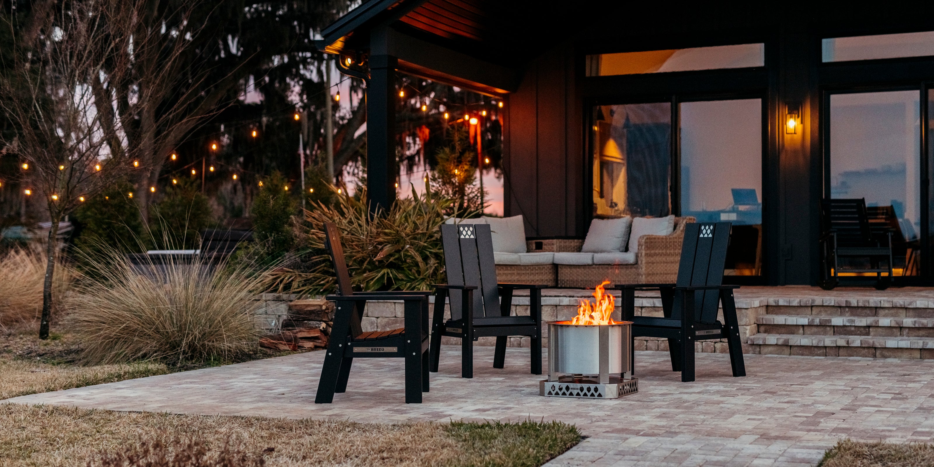 Breeo firepit and chairs on patio outside in the evening with lights on