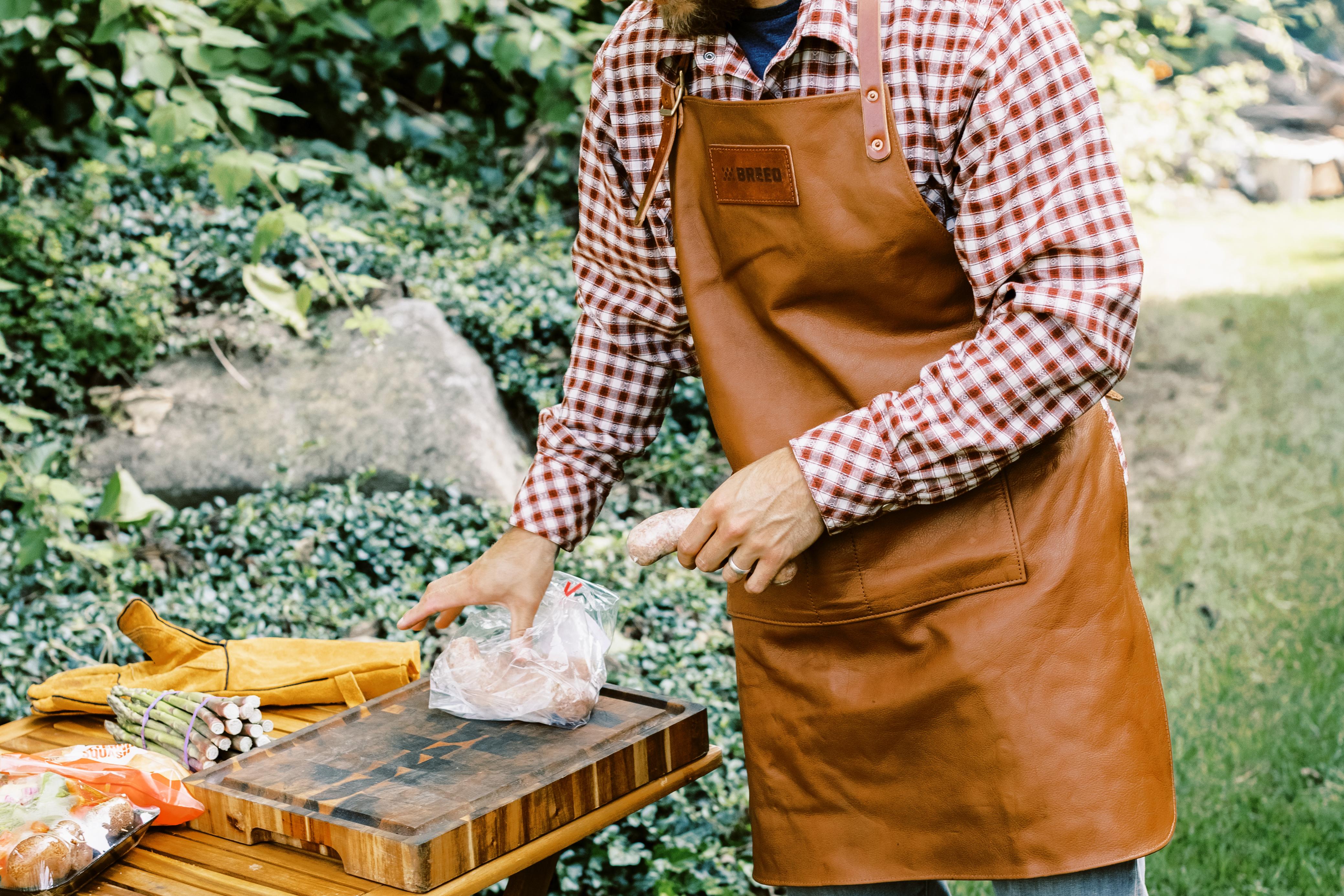 This is an image of a man wearing the Breeo Leather Grilling Apron to prep food