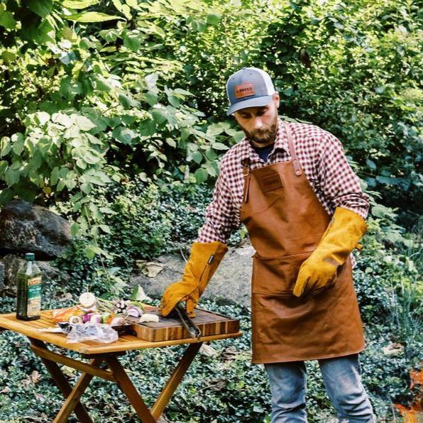 A man grilling on the X Series firepit wearing a white trucker hat