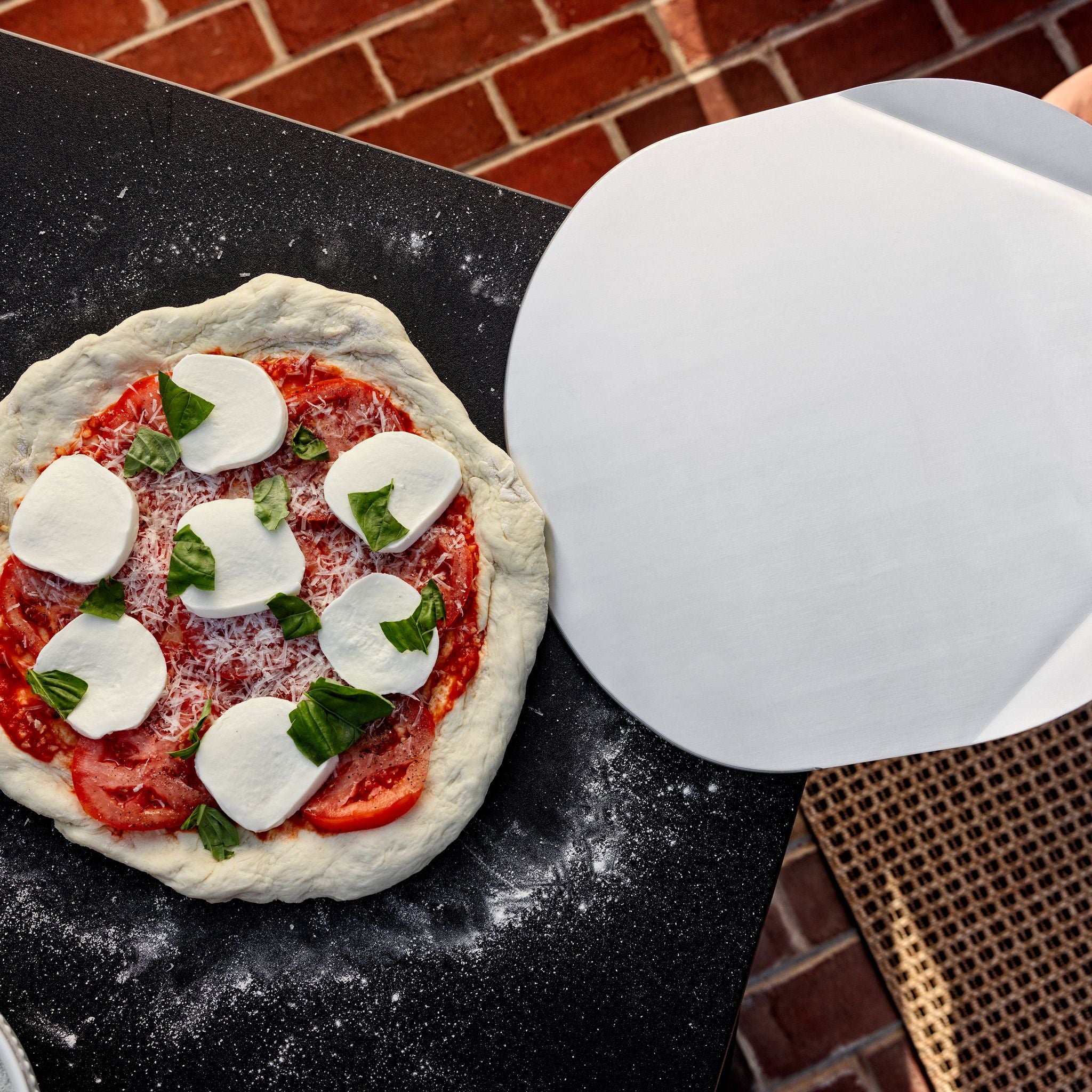A Breeo Pizza Peel transferring a pizza to an X Series Table
