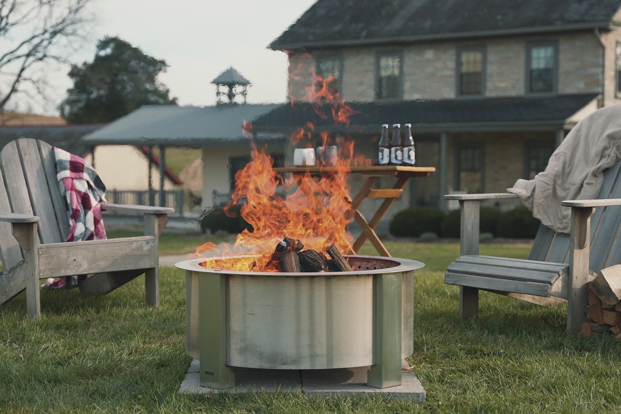 A montage video displaying X series fire pits at gatherings, cooking and grilling, insert bundles burning in stone surrounds, secondary reburn shots, Breeo Lancaster manufacturing shots.