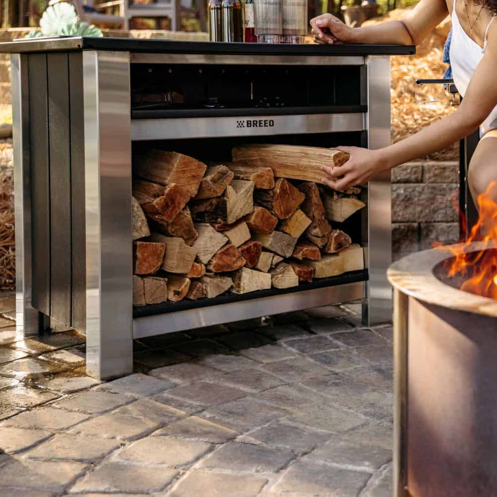 This is an image of a woman grabbing wood stored in the Breeo X Series Table