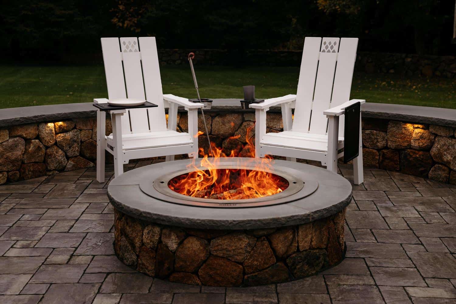 This is an image of two white X Series Chairs on a patio with an X Series Firepit inserted in a stone surround.