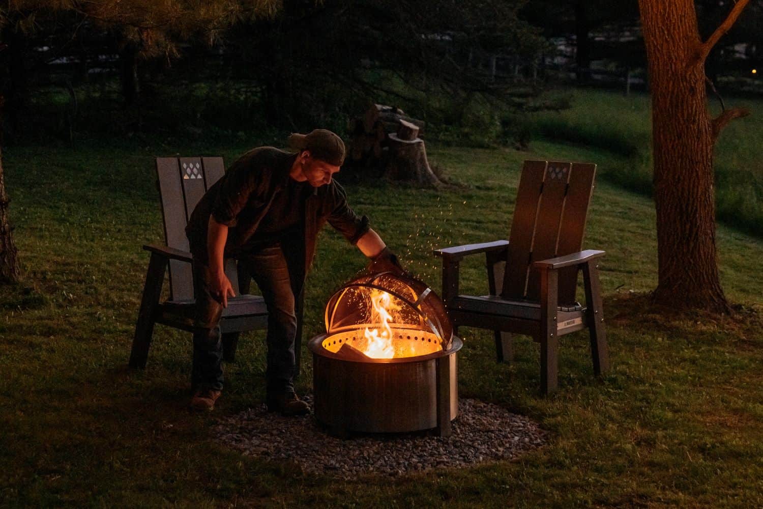 This is an image of a man closing the Spark Screen on an X Series firepit, featuring the X Series Chairs in the background.