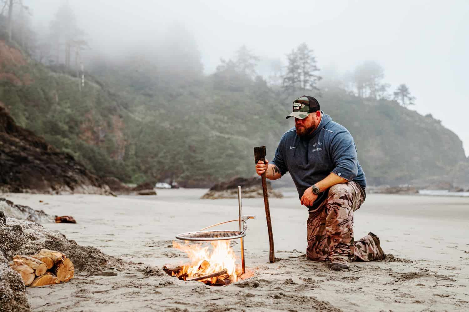 A man preparing his fire on the beach with an Outpost grill