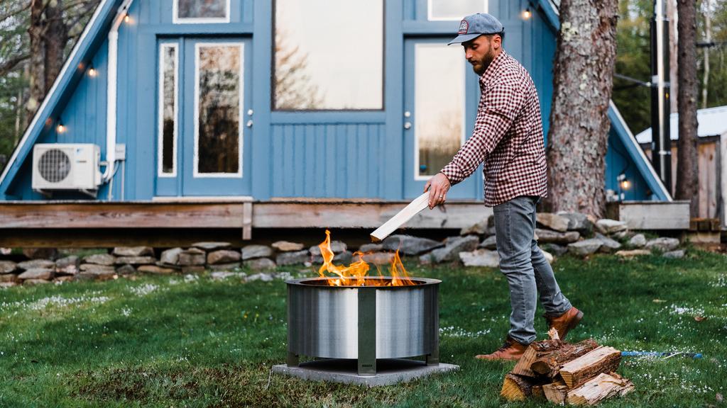 A man tossing a log into a Stainless Steel X24 Firepit 