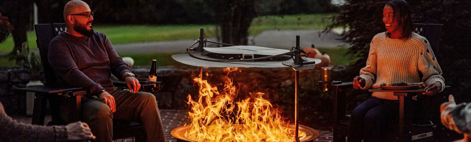 This is an image of two people enjoying the heat while sitting around an X Series 30 Firepit with a Heat Deflector 30 attached