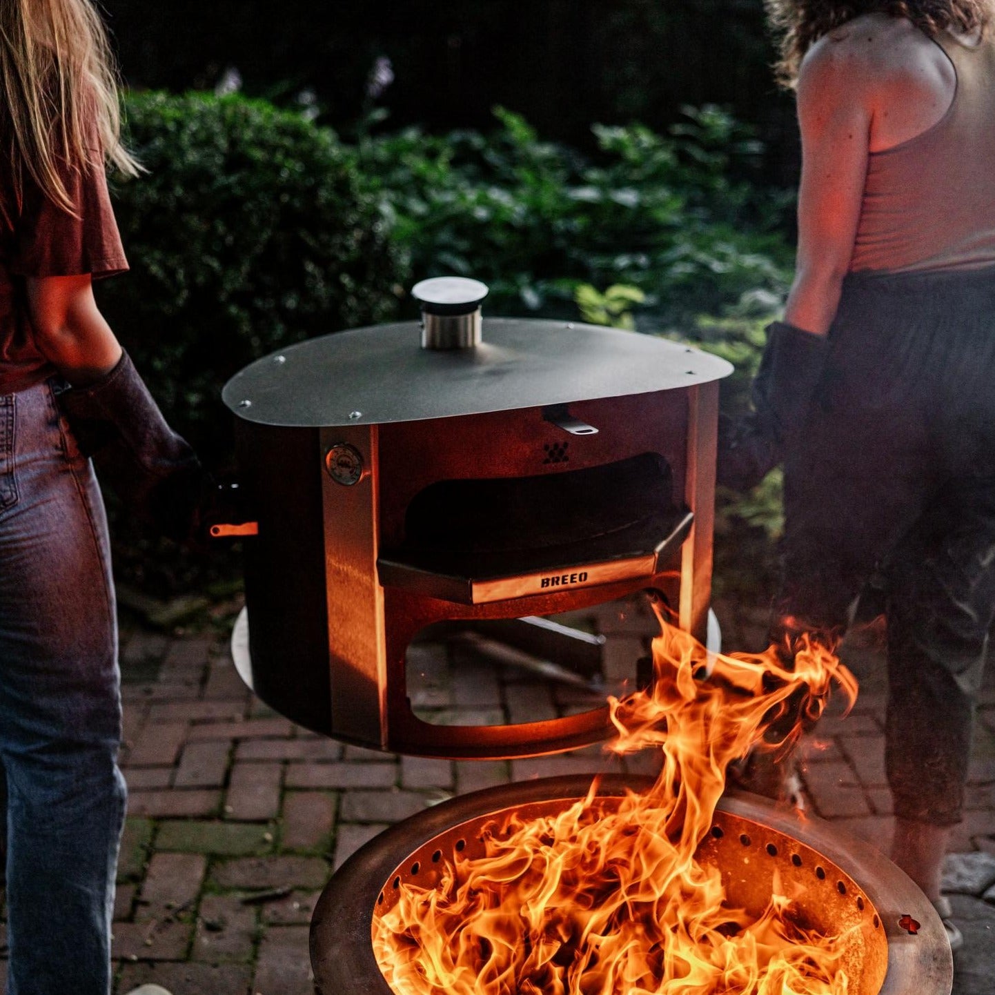 This is an image of two people removing the pizza oven from the firepit