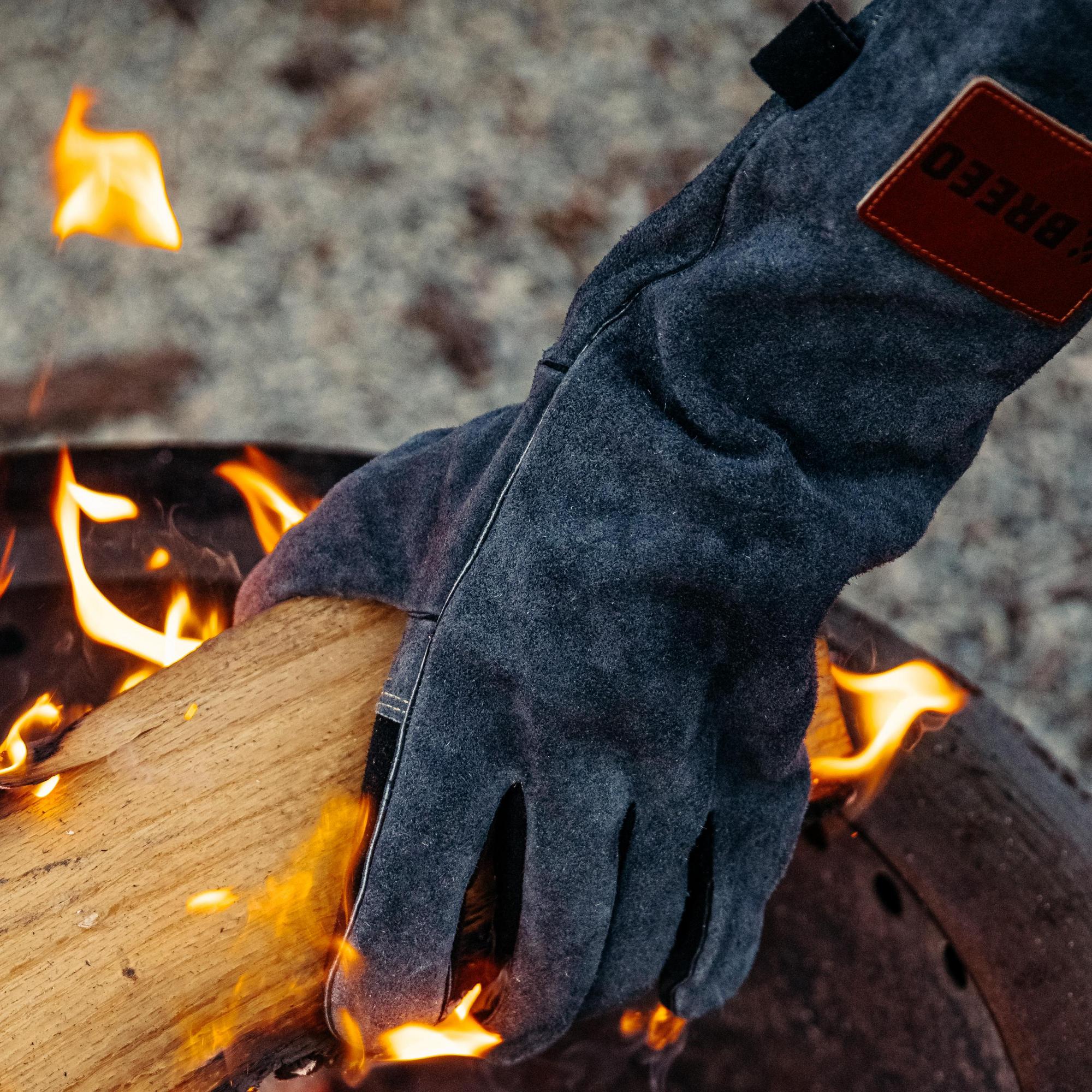 This is an image of a person wearing the Breeo leather fire gloves to remove a log from the fire