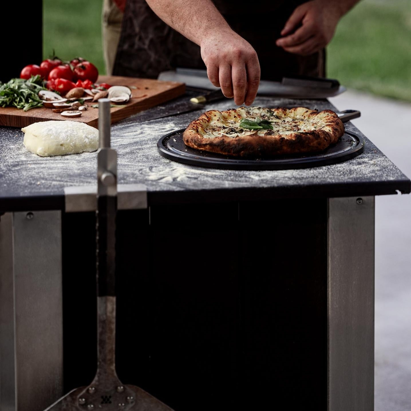 This is an image of a man sprinkling toppings on a fresh baked pizza on the Serving Board