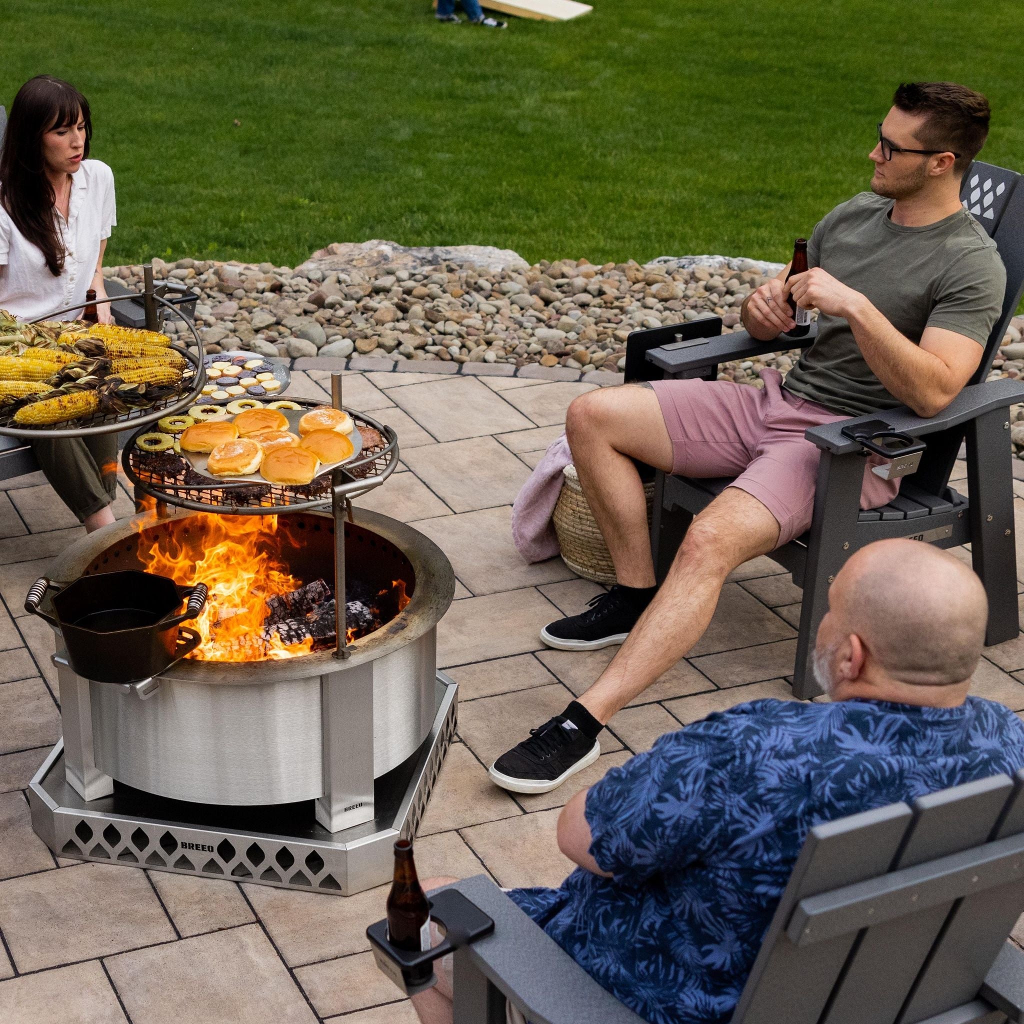 An image of friends grilling around an X Series firepit with X Series Chairs and Outrig cupholders attached.