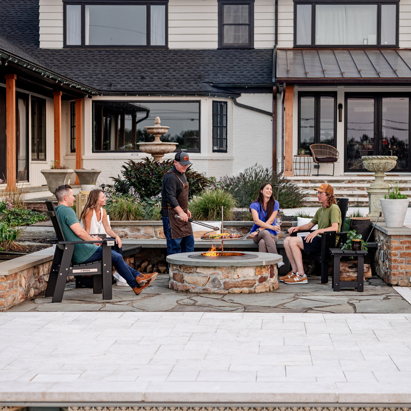 A group of friends hanging out and sitting around the Zentro fire pit cooking on an outpost grill
