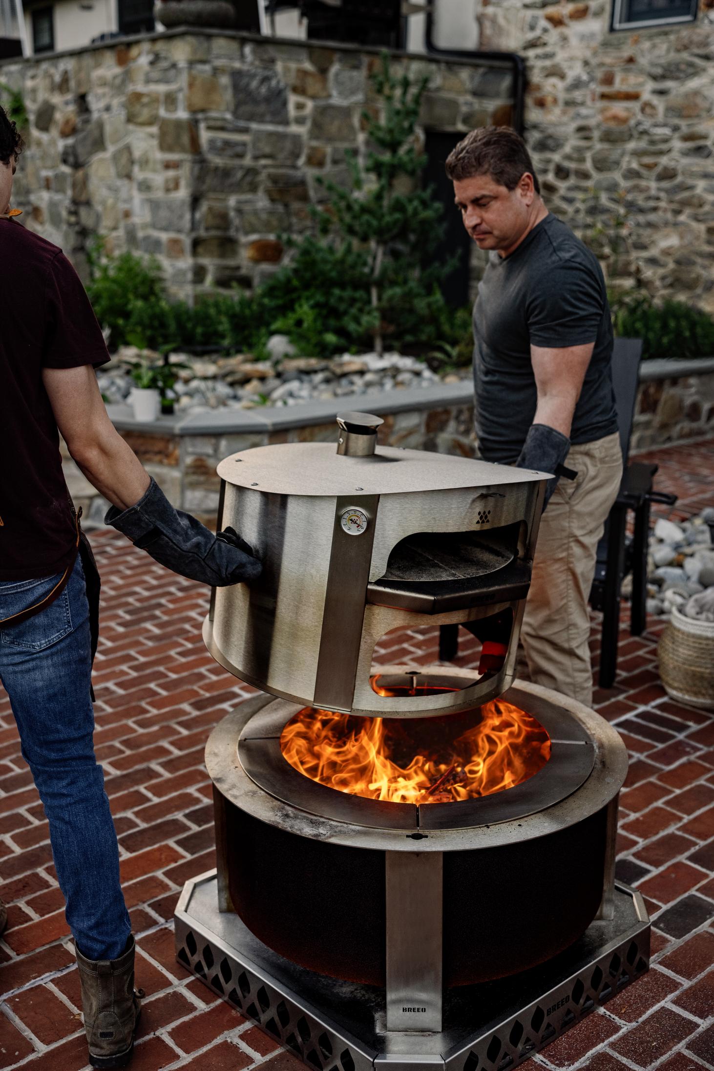 This is an image of two men moving a pizza oven from the firepit