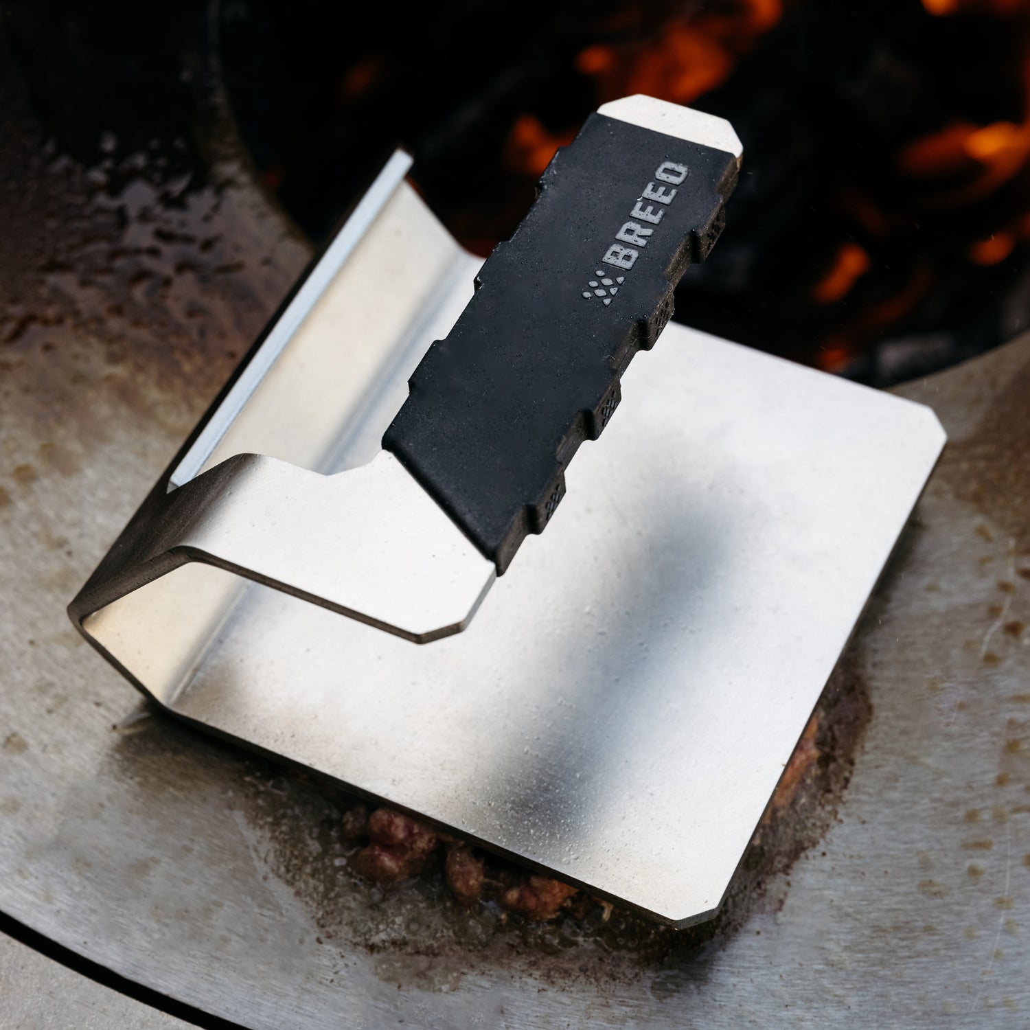 A Griddle Press sits on a sear-plate with coals visible below.