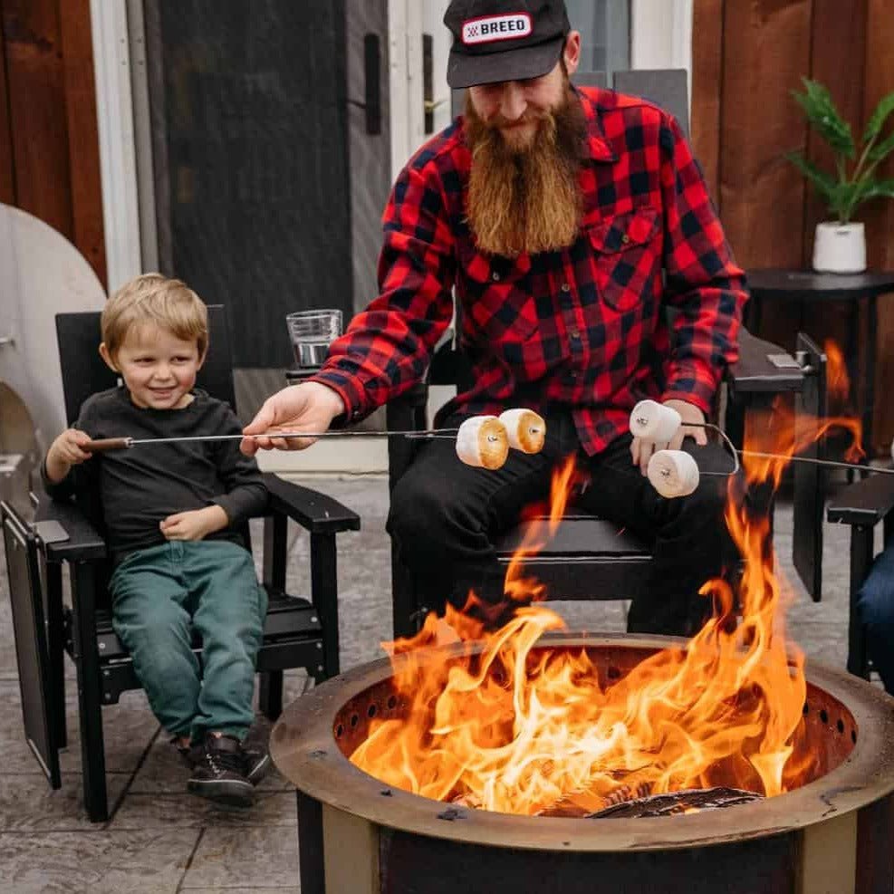 This is an image of a Father roasting marshmallows with his kids while sitting on Breeo chairs around the fire