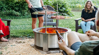 A group of friends gathered around a Breeo firepit grilling hamburgers. 