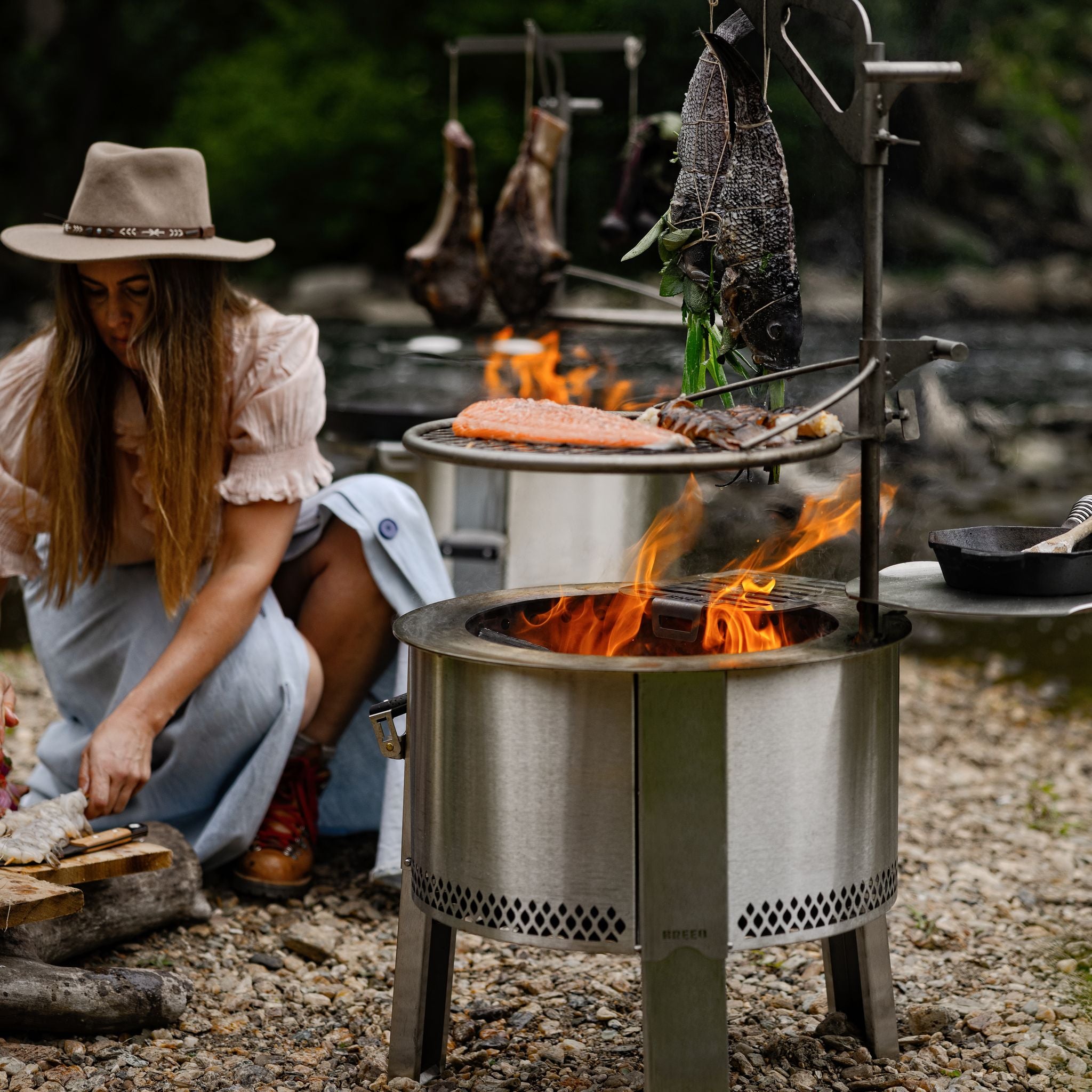 A woman cooking fish and steaks over the Y Series firepit with grilling accessories. 